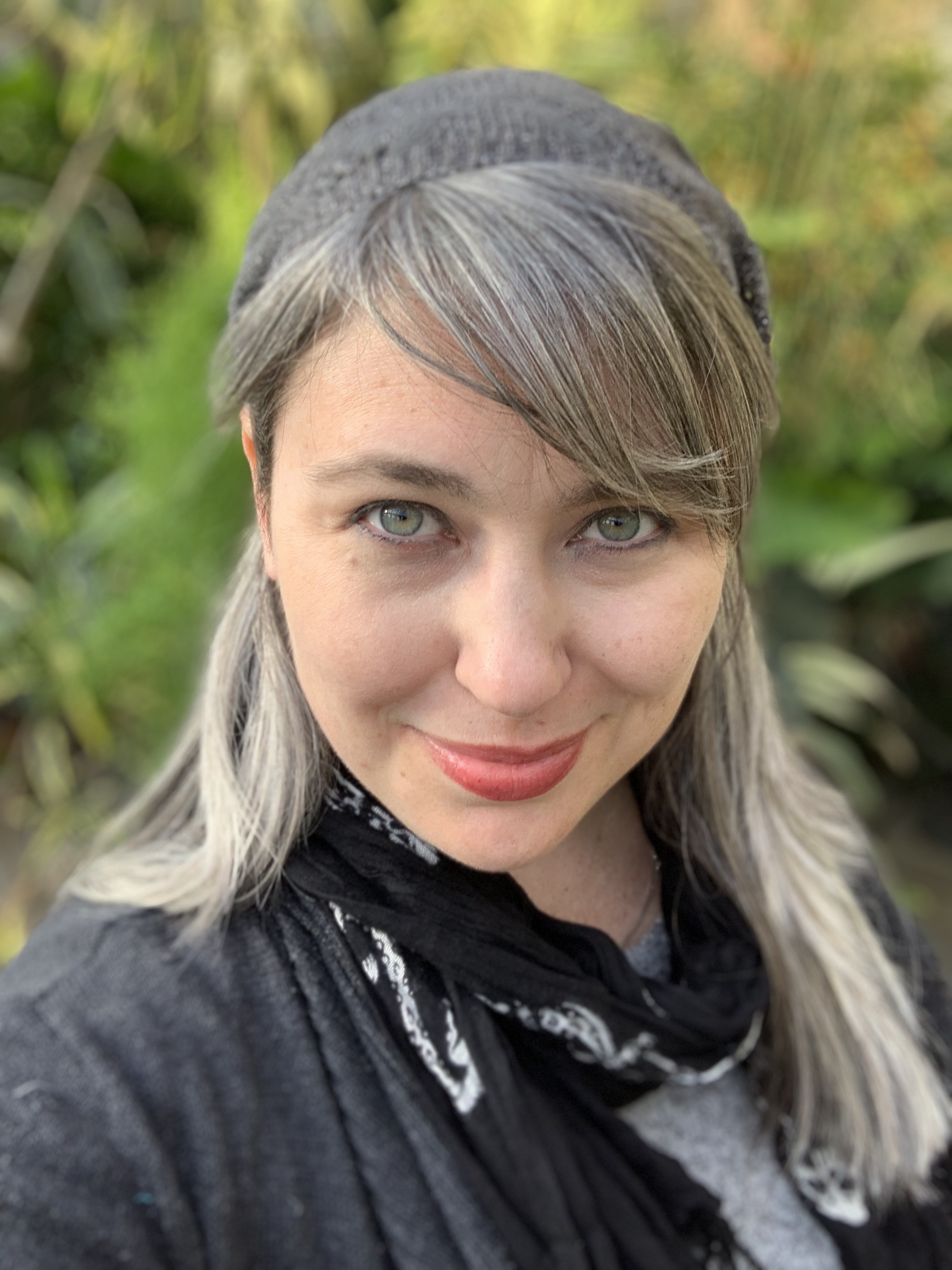 Lexi Lavene, silver-haired author in a black knit hat, smiling in the woods